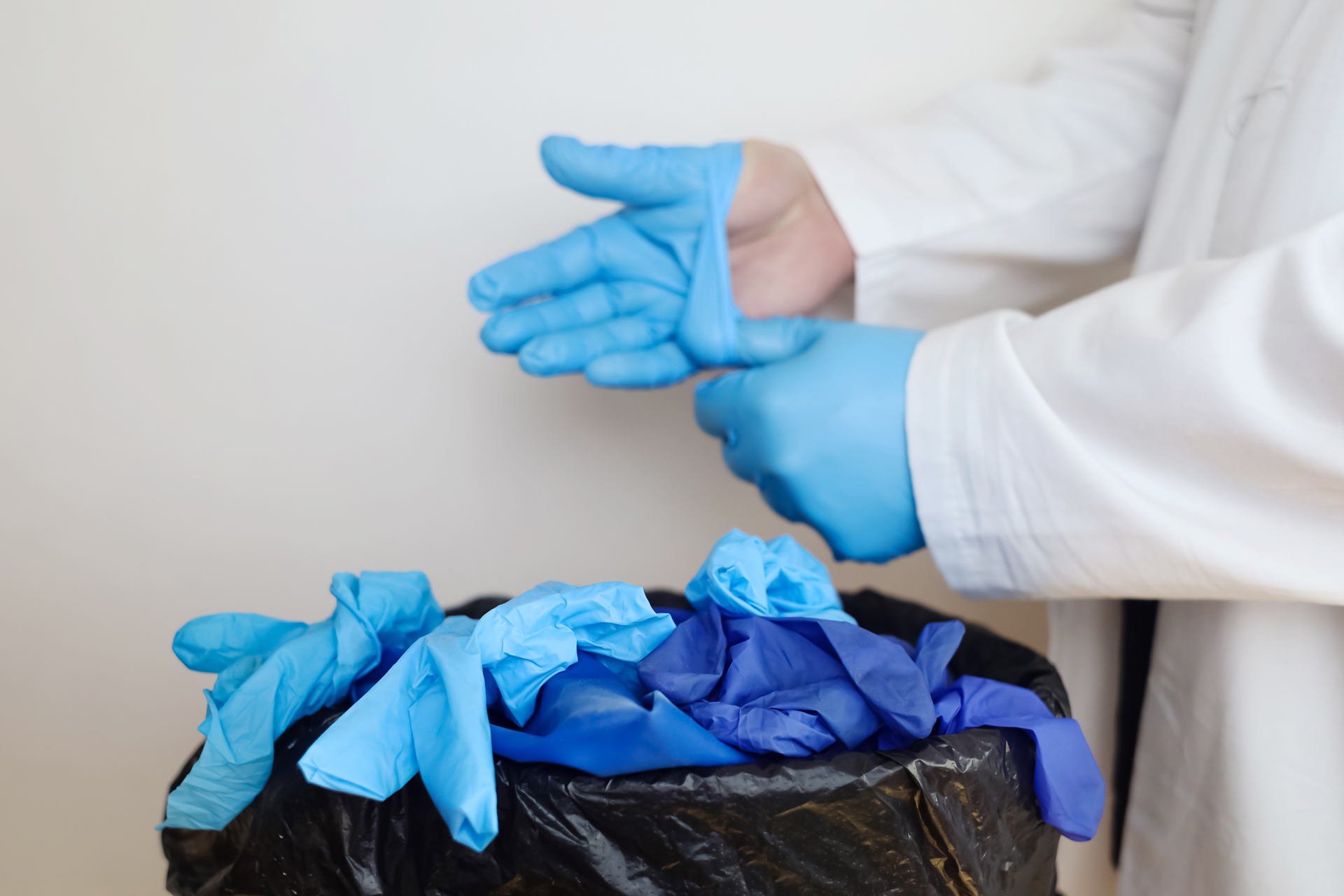 Doctor removing blue plastic gloves and throwing them in the bin