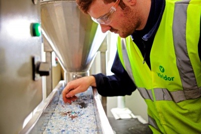 An image of a man in high vis leaning over a tray of plastic pellets