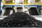 Granulated black mass from battery recycling piled in the foreground of a industrial recycling facility