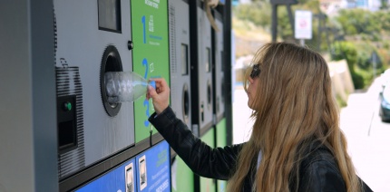 Female student putting a plastic bottle into a deposit return machine