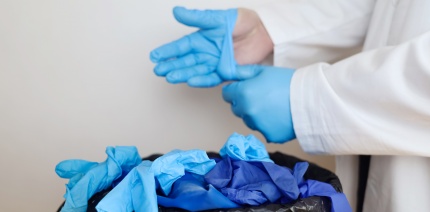 Doctor removing blue plastic gloves and throwing them in the bin